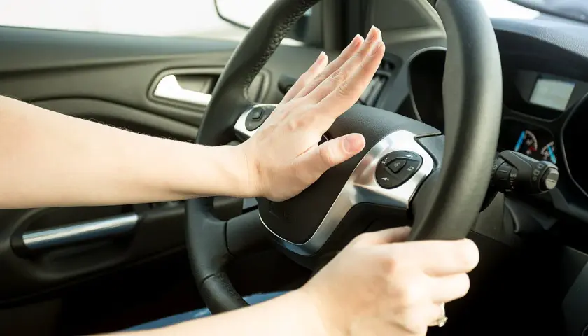 Hand drückt Hupe am Lenkrad. Darf man mit defekter Hupe fahren? Das ist eine wichtige Frage für die Verkehrssicherheit.