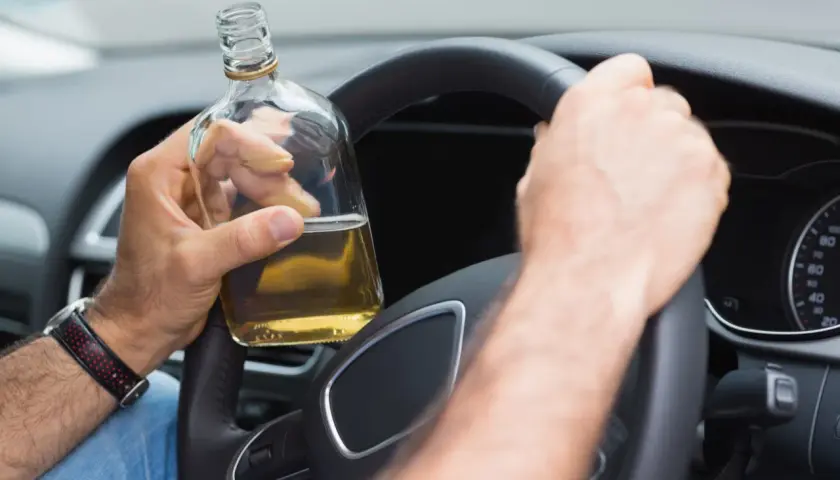 Mann hält Flasche Alkohol am Steuer. 2 Promille wieviel Alkohol? Gefährliche Fahrt.