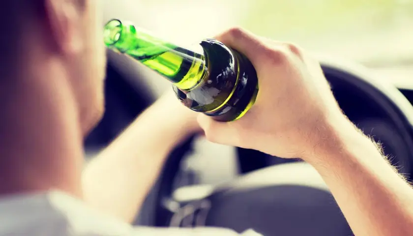 Mann hält Flasche im Auto, ignoriert die Promillegrenze beim Autofahren.