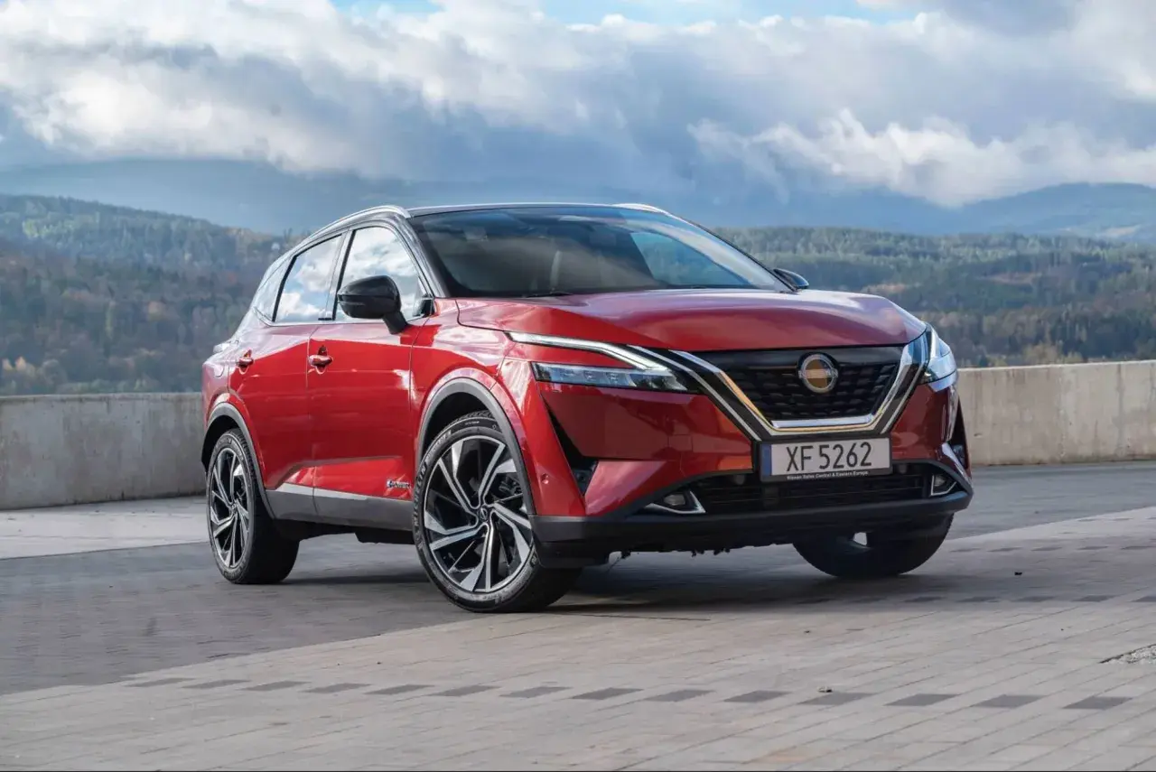 Roter Nissan Qashqai vor einer bergigen Landschaft. Die Frage "woher kommt Nissan" wird durch die Herkunft des Autos beantwortet: aus Japan.