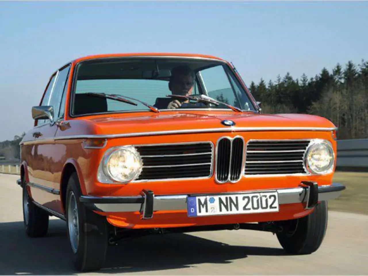 Ein leuchtend orangefarbener BMW 2002, ein Kultauto der 70er Jahre, fährt auf einer Landstraße.