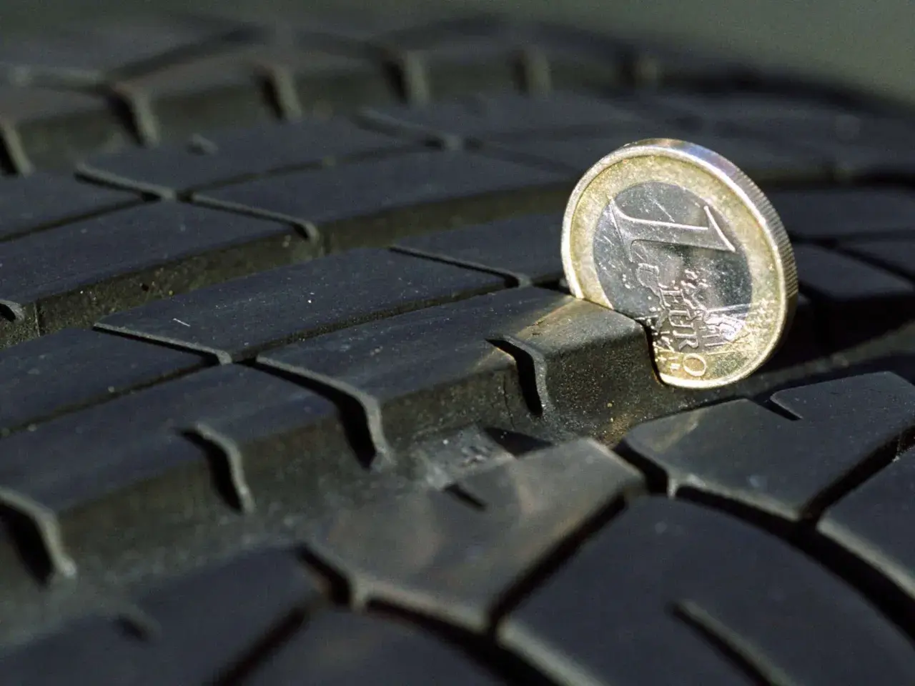 Ein 1-Euro-Stück ragt aus dem Profil eines abgefahrenen Reifens. Das zeigt, dass abgefahrene Reifen eine Strafe nach sich ziehen können.
