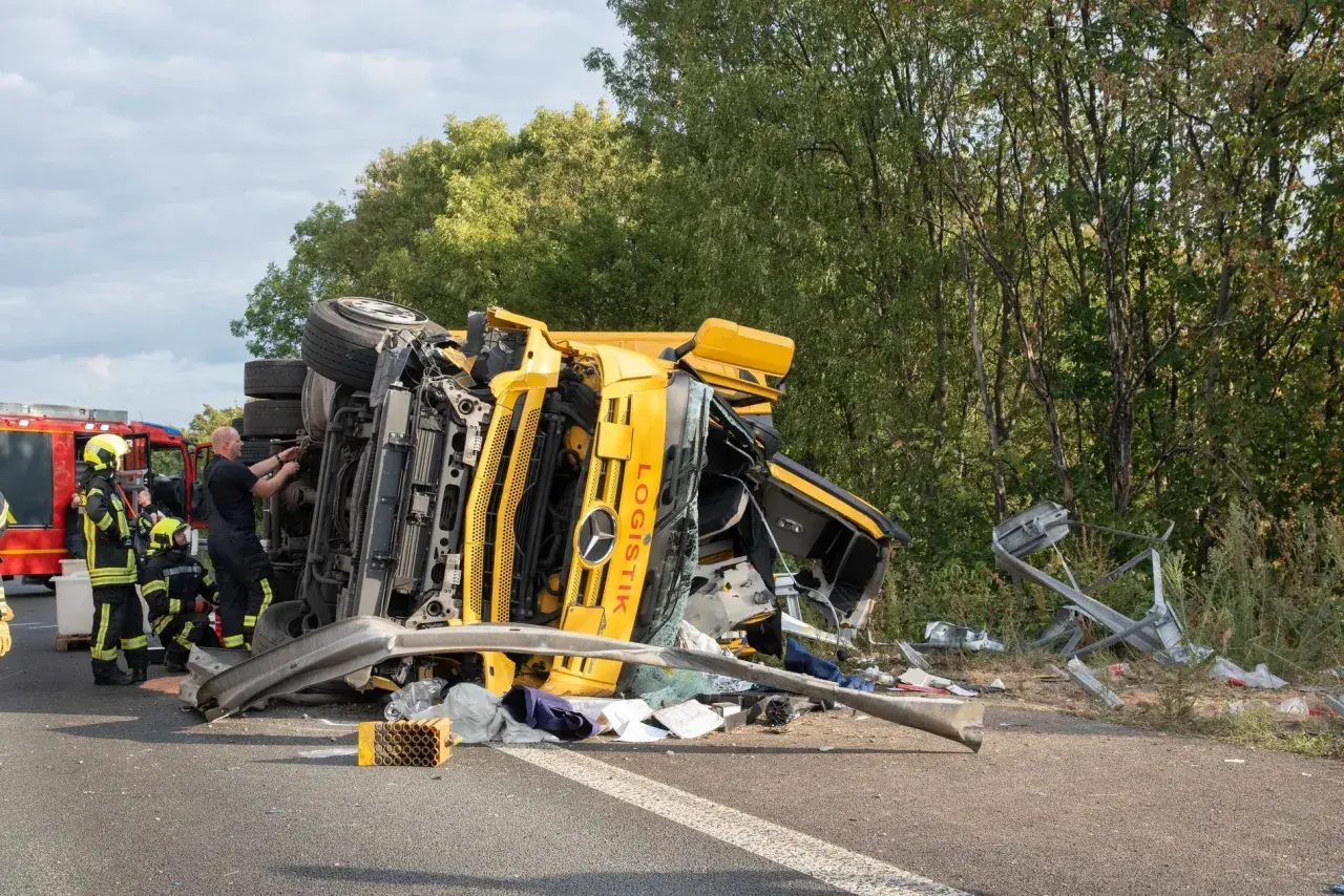 Umgekippter gelber LKW nach Unfall auf der A57. Feuerwehrleute sichern die Unfallstelle.