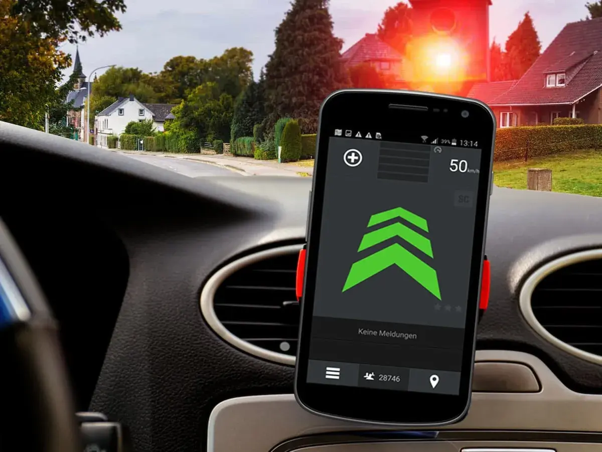Smartphone mit Blitzer-App für Android Auto zeigt 50 km/h. Im Hintergrund rote Ampel und Häuser.
