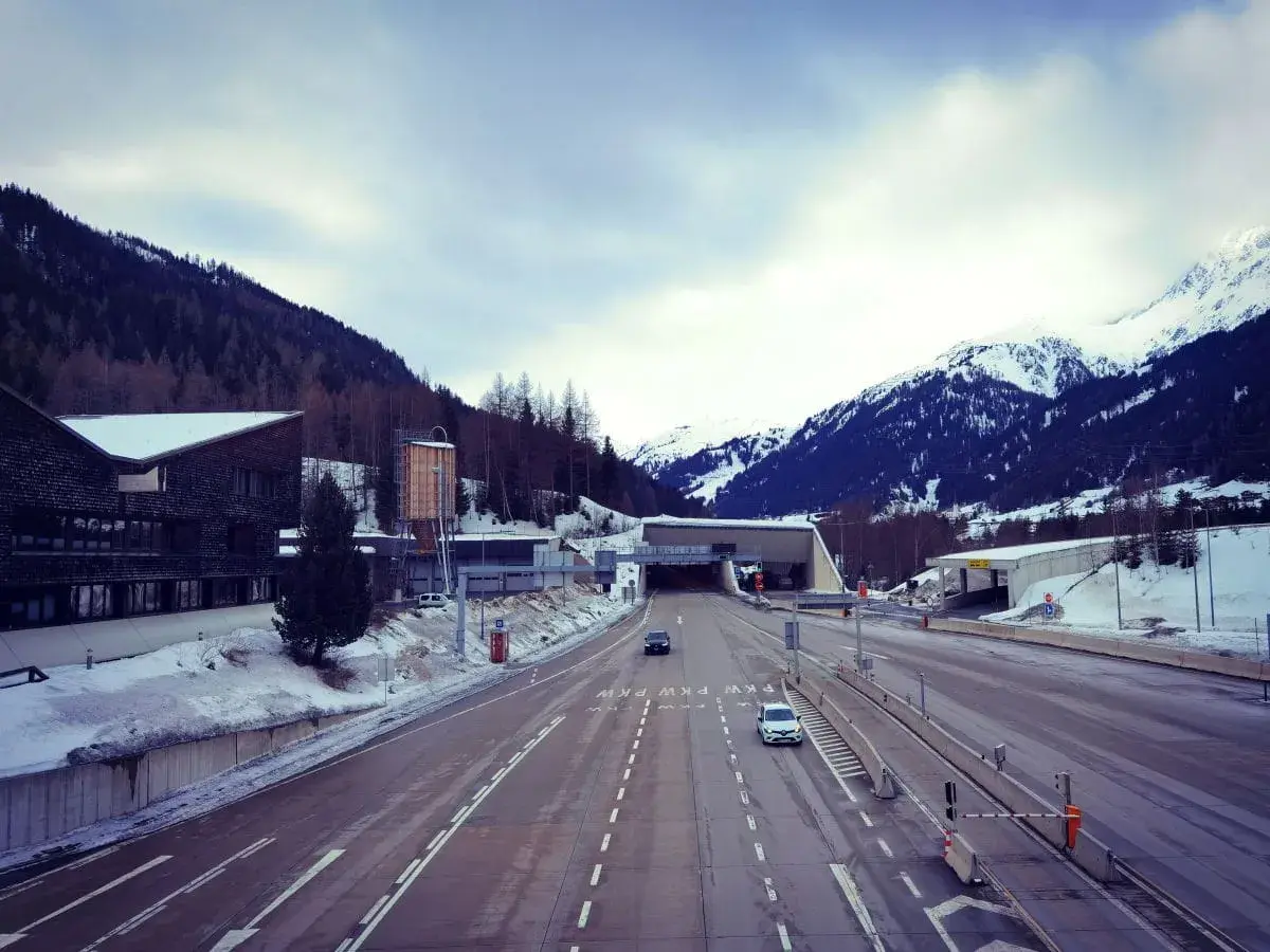 Winterliche Fahrt zum Arlbergpass. Ein Wohnwagen parkt neben der Straße, während Autos in den Tunnel fahren.