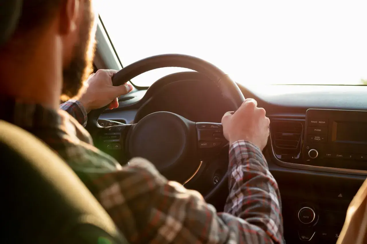 Mann mit Bart fährt Auto, Hände am Lenkrad. Er möchte sein Fahrverbot umwandeln und genießt die Fahrt.