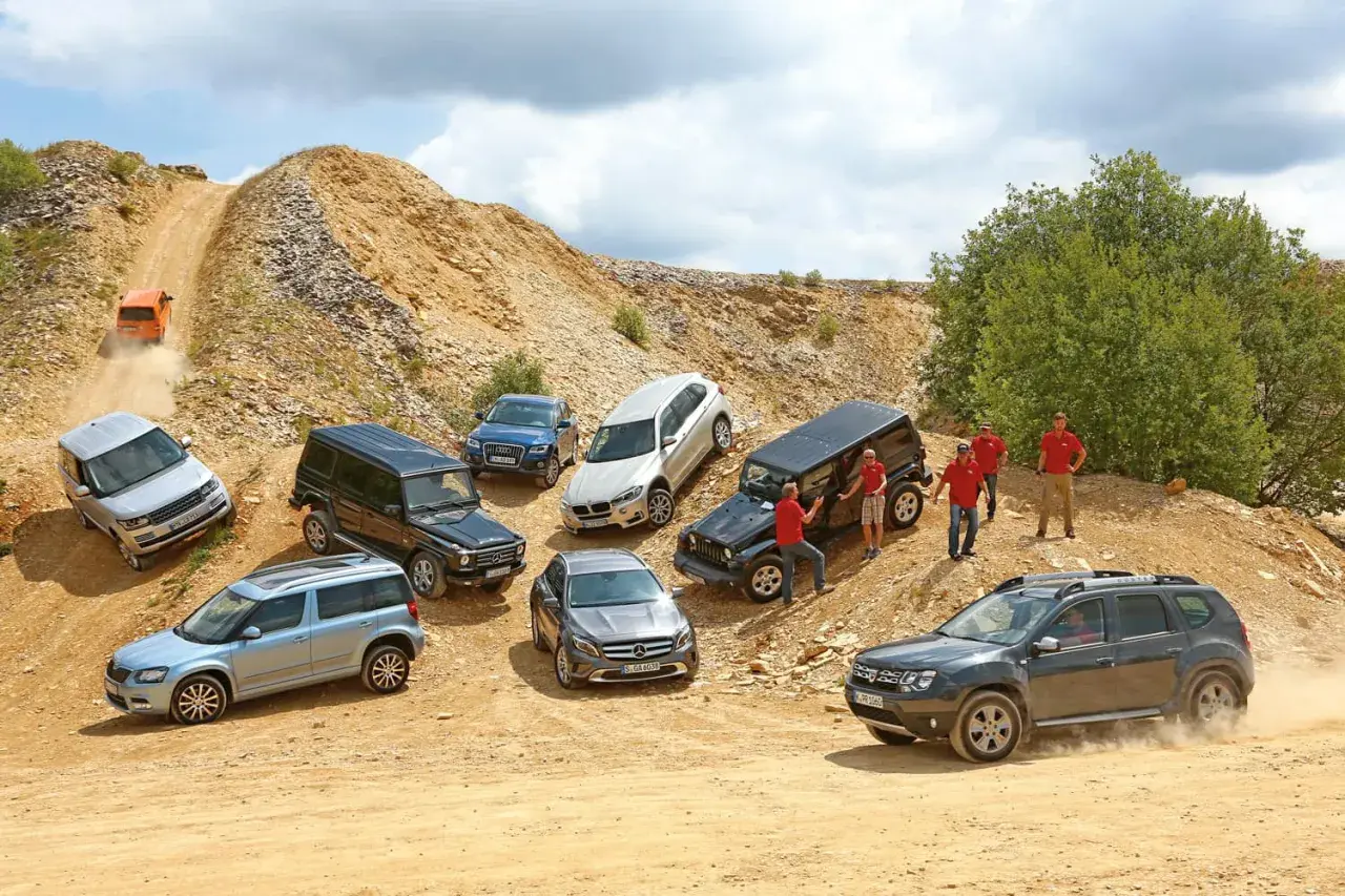 Verschiedene SUVs und Geländewagen auf einer Schotterpiste. Ein orangefarbener Wagen fährt einen steilen Hang hinauf. Das zeigt, was bedeutet offroad.