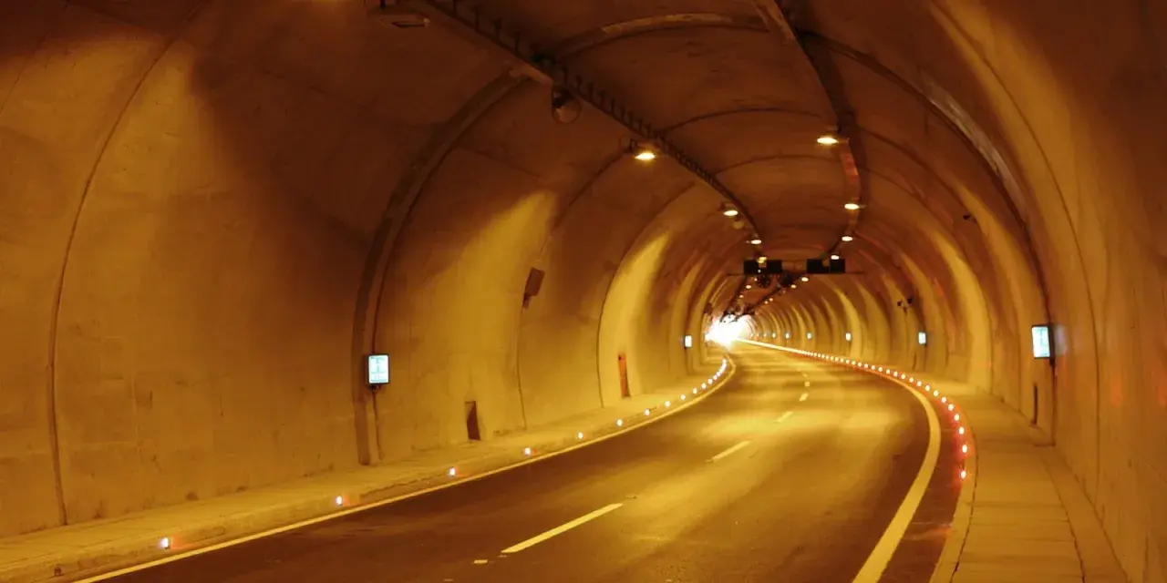 Die A10 Tauernautobahn führt durch einen beleuchteten Tunnel. Die Straße ist nass, die Wände sind aus Beton und mit Lichtern versehen.