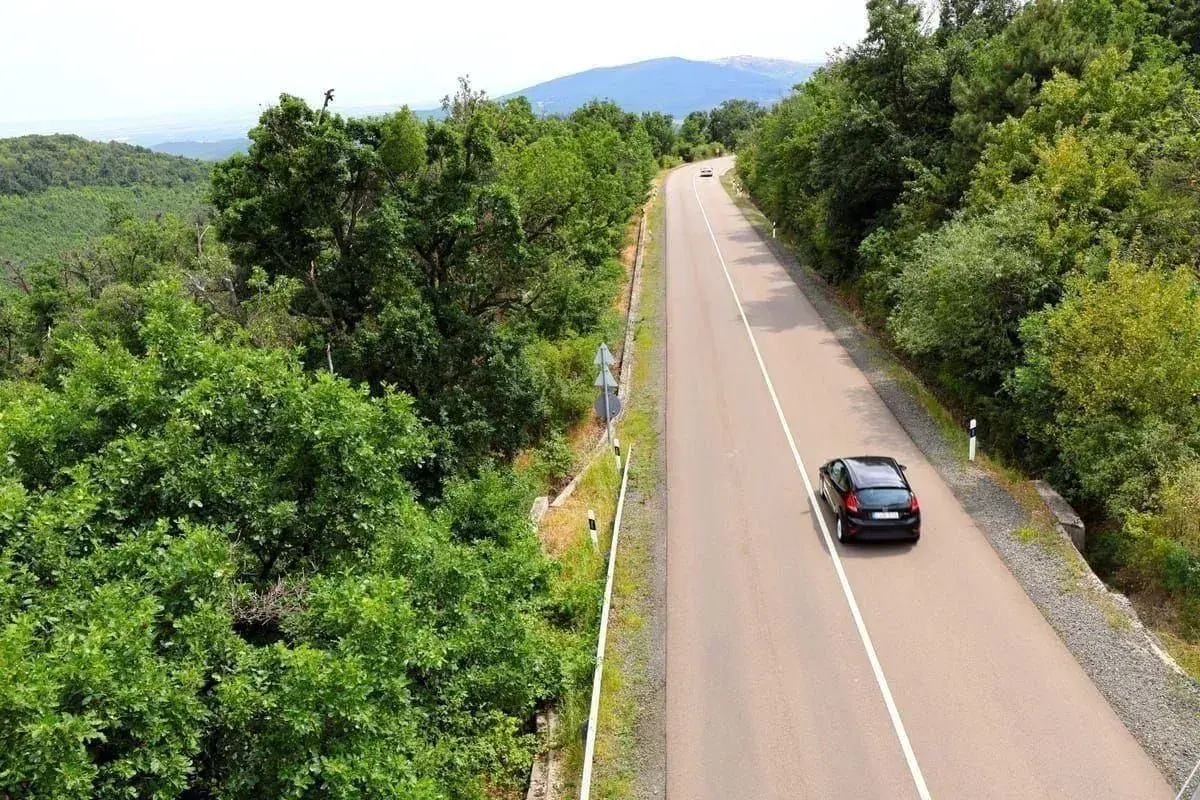 Autofahren in Kroatien auf einer kurvigen Straße durch üppige grüne Wälder, mit einem schwarzen Auto, das bergauf fährt.