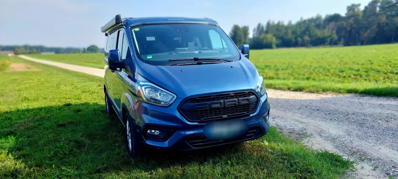 Blauer Campervan (Westfalia) steht auf einer Wiese neben einem Feldweg. Hoffentlich keine uebler i21 probleme auf der Reise!