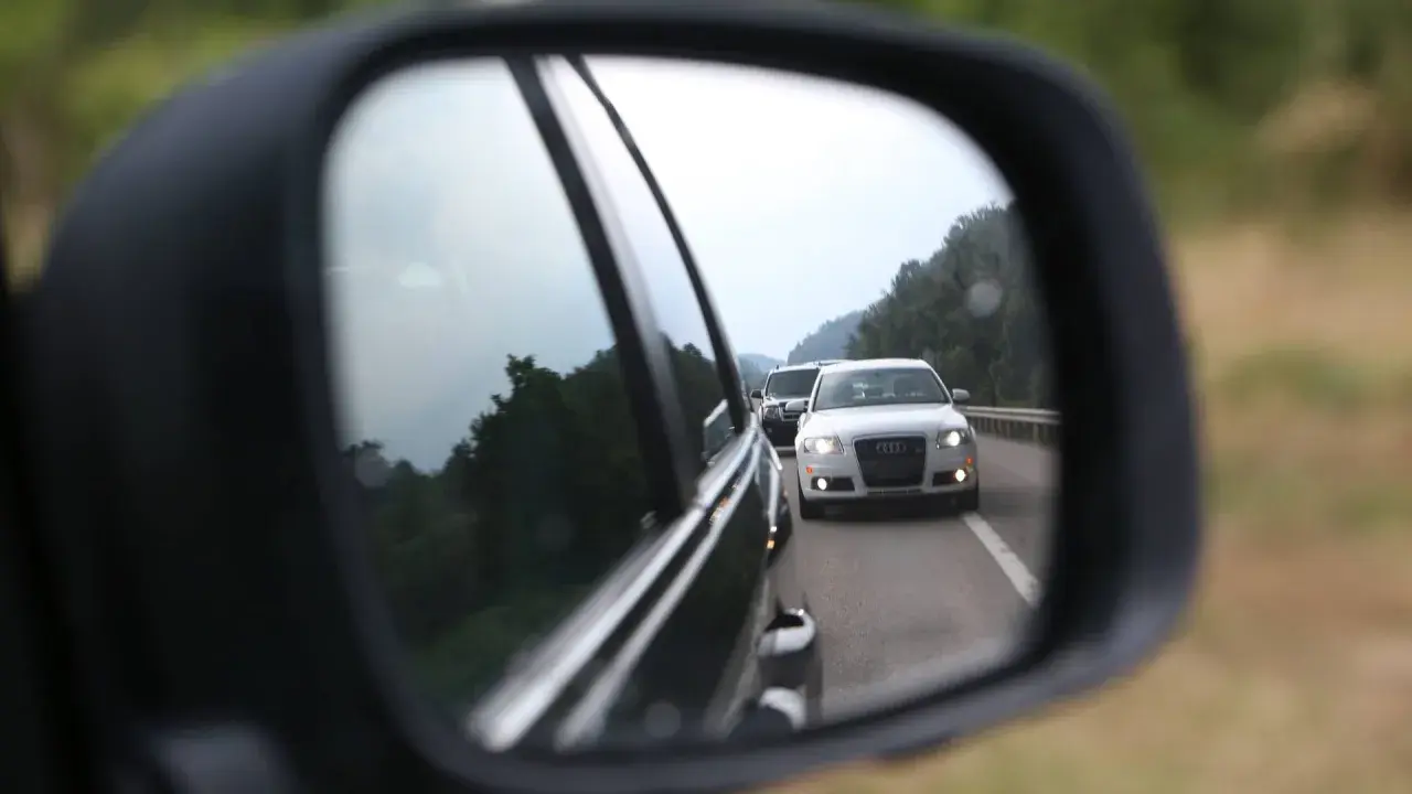 Rückspiegel zeigt weiße Audi-Limousine auf der Autobahn, die Lichthupe gibt.