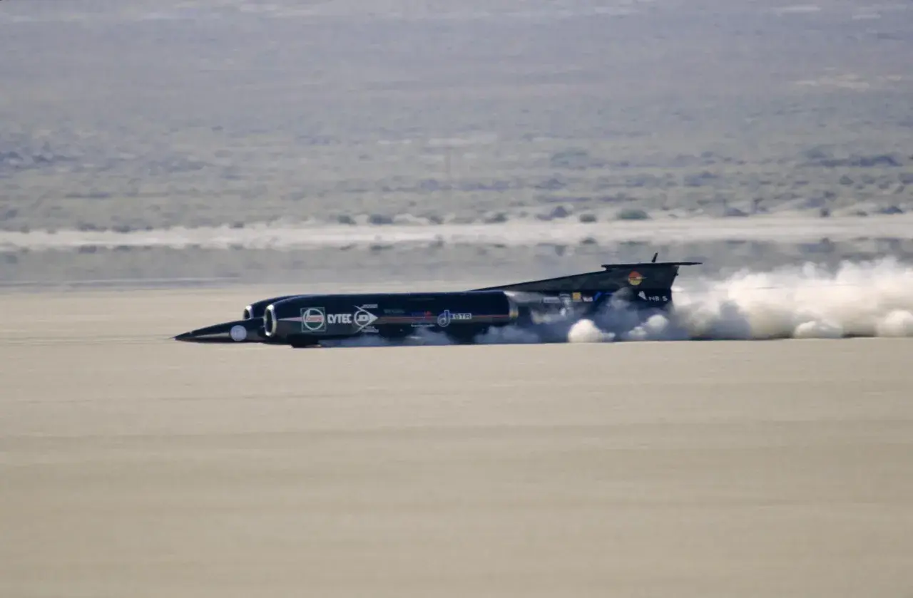 Schwarzes Raketenauto, das mit enormem Schub über eine trockene Ebene rast und eine Staubwolke hinterlässt. Der Thrust SSC ist ein Meisterwerk der Ingenieurskunst.