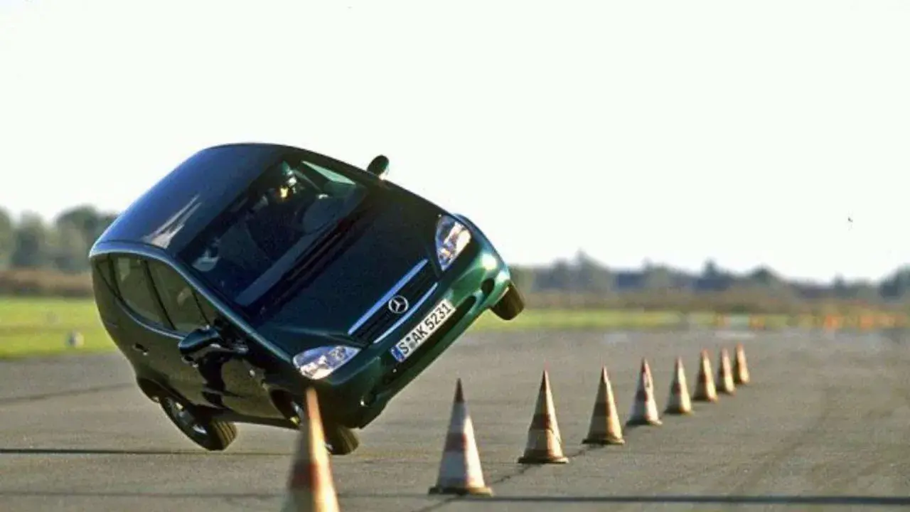 Ein grüner Kleinwagen kippt im Elchtest gefährlich zur Seite, während er eine Reihe von Pylonen umfährt.