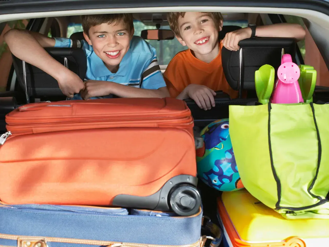 Zwei lächelnde Jungen schauen über Koffer und Taschen im Kofferraum. Die Koffer sind gepackt, die reise checkliste ist abgehakt.