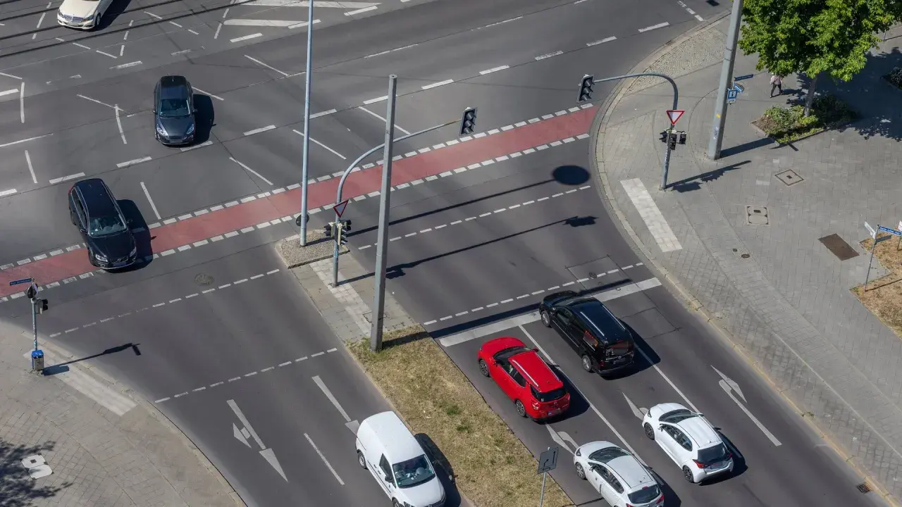 Autos warten an einer Kreuzung für mehrspuriges Abbiegen. Ein roter Kleinwagen und ein schwarzer Van sind zu sehen.
