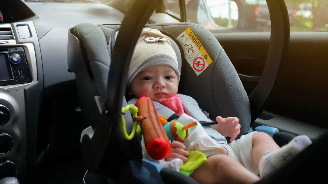 Ein Baby im Kindersitz vorne im Auto. Die Frage "ab wann darf ein Kind vorne sitzen" ist hier relevant, da es auf die richtige Sicherung ankommt.