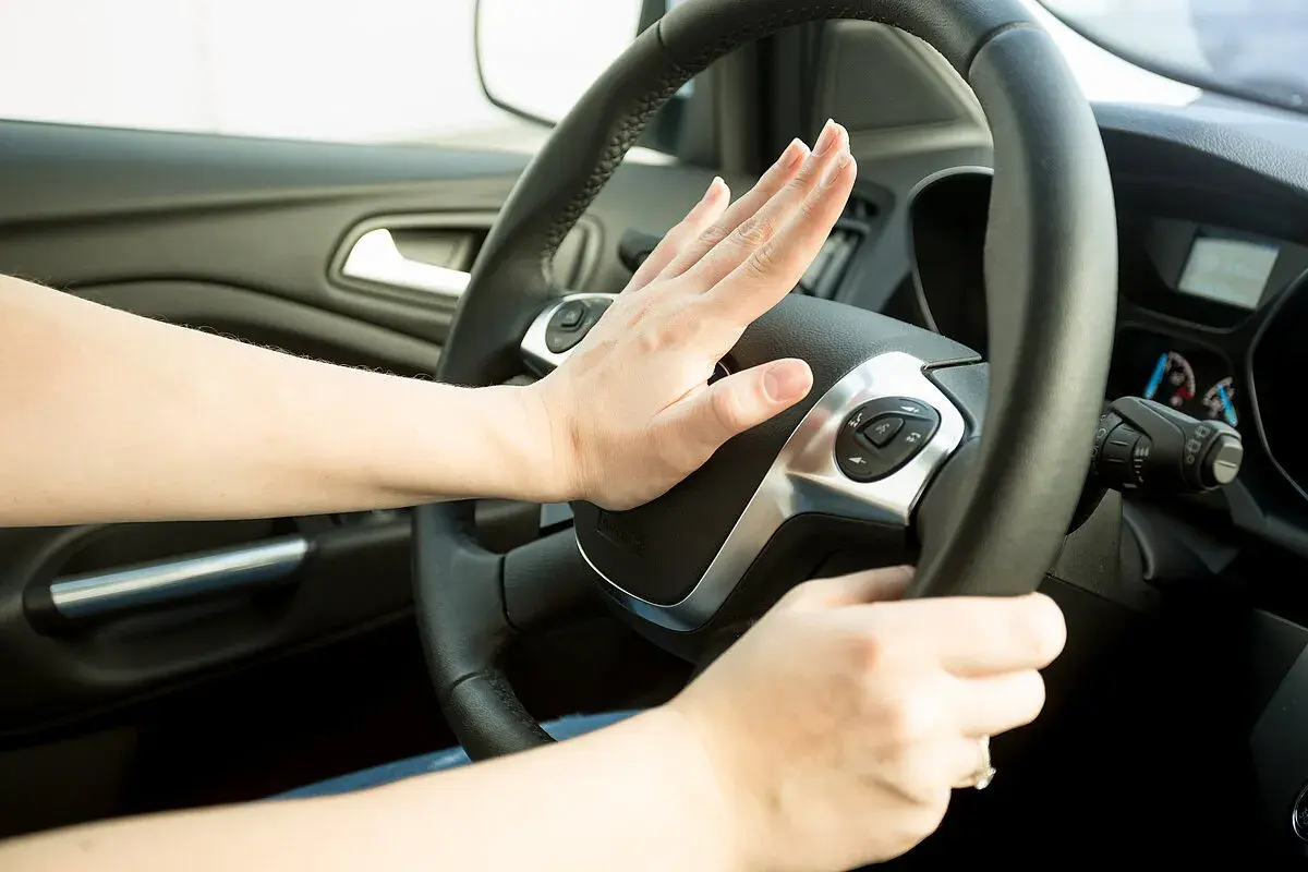 Hand drückt Hupe am Lenkrad. Darf man mit defekter Hupe fahren? Das ist eine wichtige Frage für die Verkehrssicherheit.