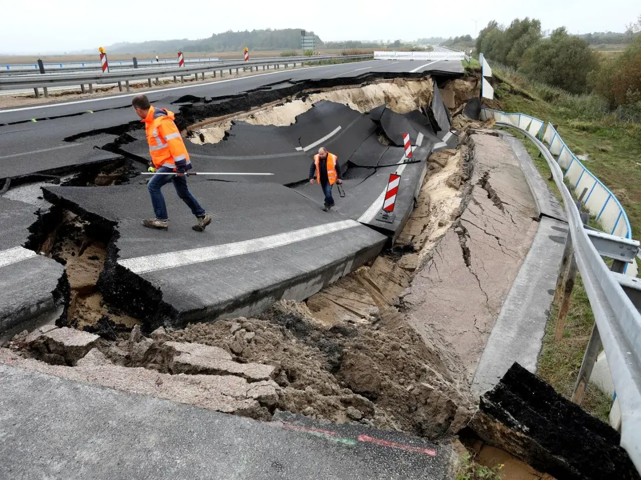 Zwei Männer in Warnwesten inspizieren eine eingestürzte Autobahn A20. Der Asphalt ist aufgebrochen und klafft tief.