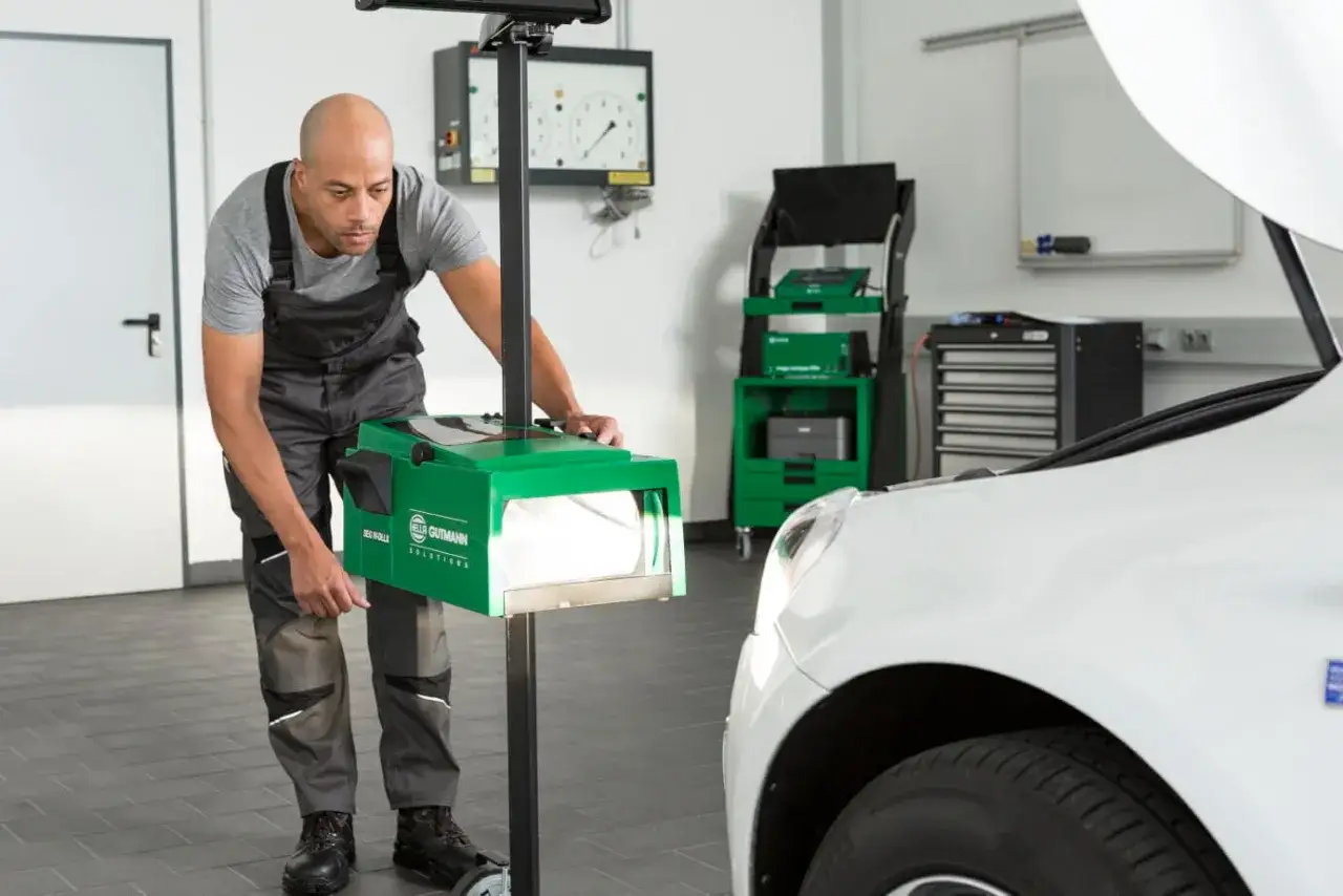 Werkstattmitarbeiter stellt mit einem Messger&auml;t die automatische Leuchtweitenregulierung eines Autos ein.
