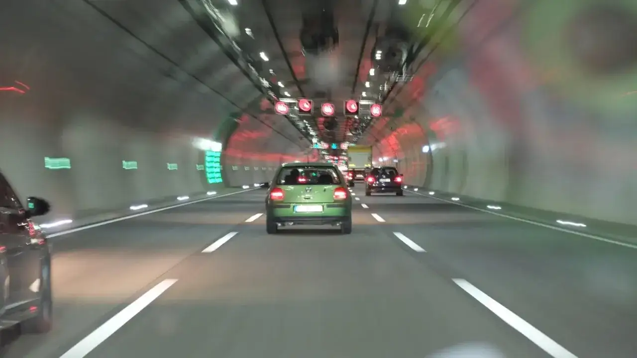 Fahrt durch einen Tunnel mit Autos. Über der Fahrbahn sind rote Schilder mit Geschwindigkeitsbegrenzungen zu sehen, die wie ein infrarot blitzer wirken.