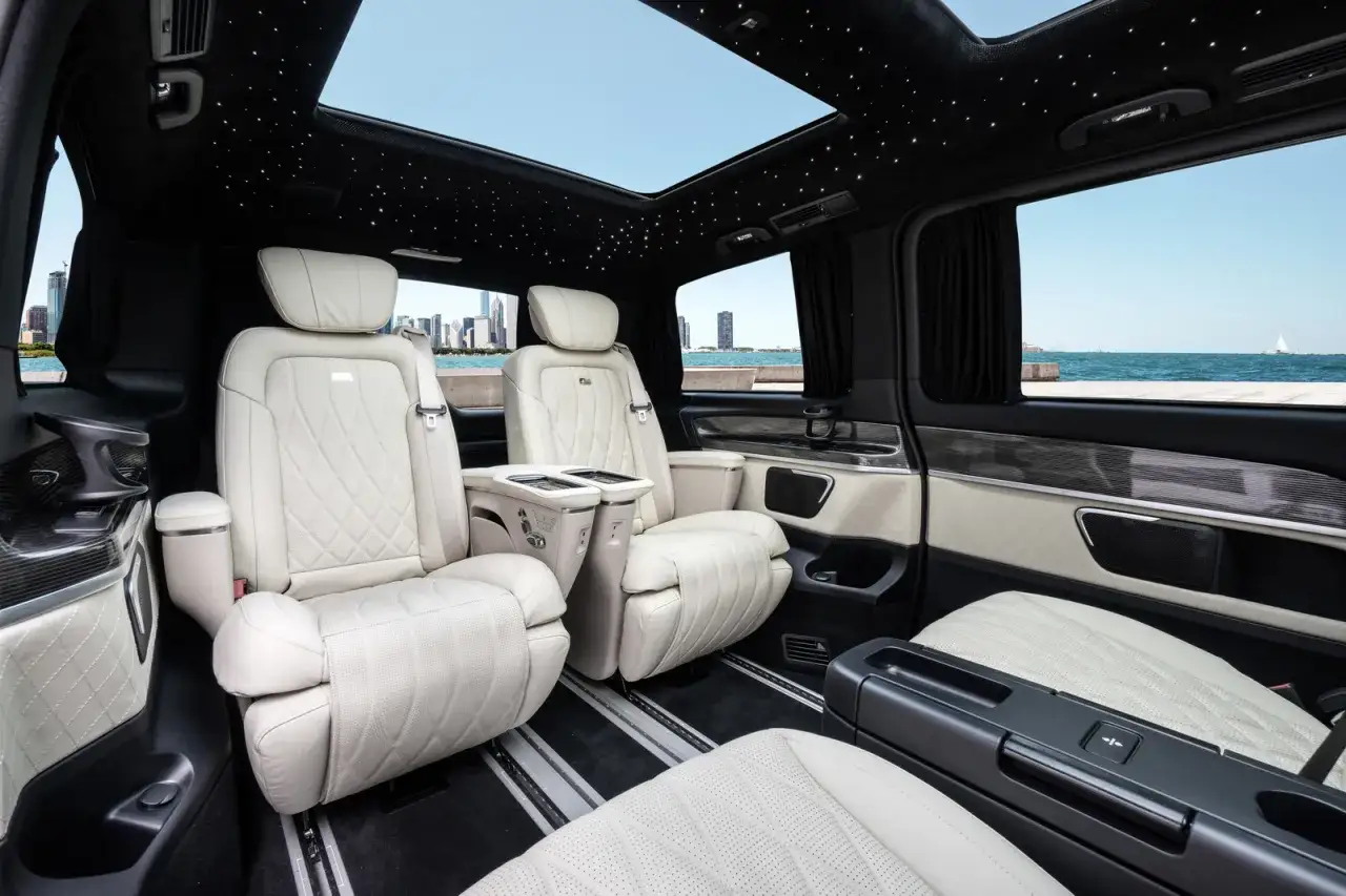Luxuri&ouml;ses Interieur eines Van-Autos mit bequemen Ledersitzen, Sternenhimmel und Blick auf eine Stadt am Wasser.