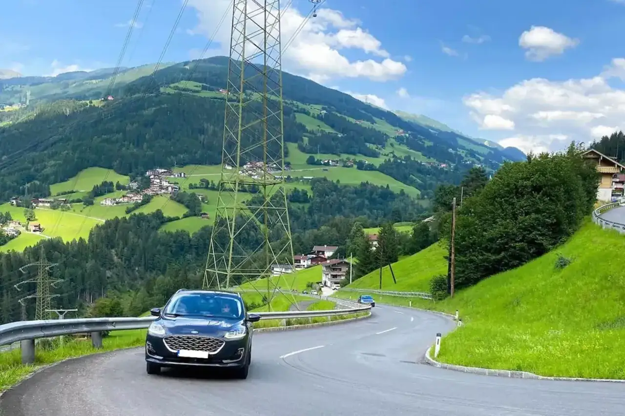 Autofahrt durch eine gr&uuml;ne Berglandschaft mit Strommasten. Die Stra&szlig;e schl&auml;ngelt sich durch das Tal, vorbei an H&auml;usern und Wiesen. Vielleicht ist dies die Route, um die Lichtenstein Maut zu umgehen.