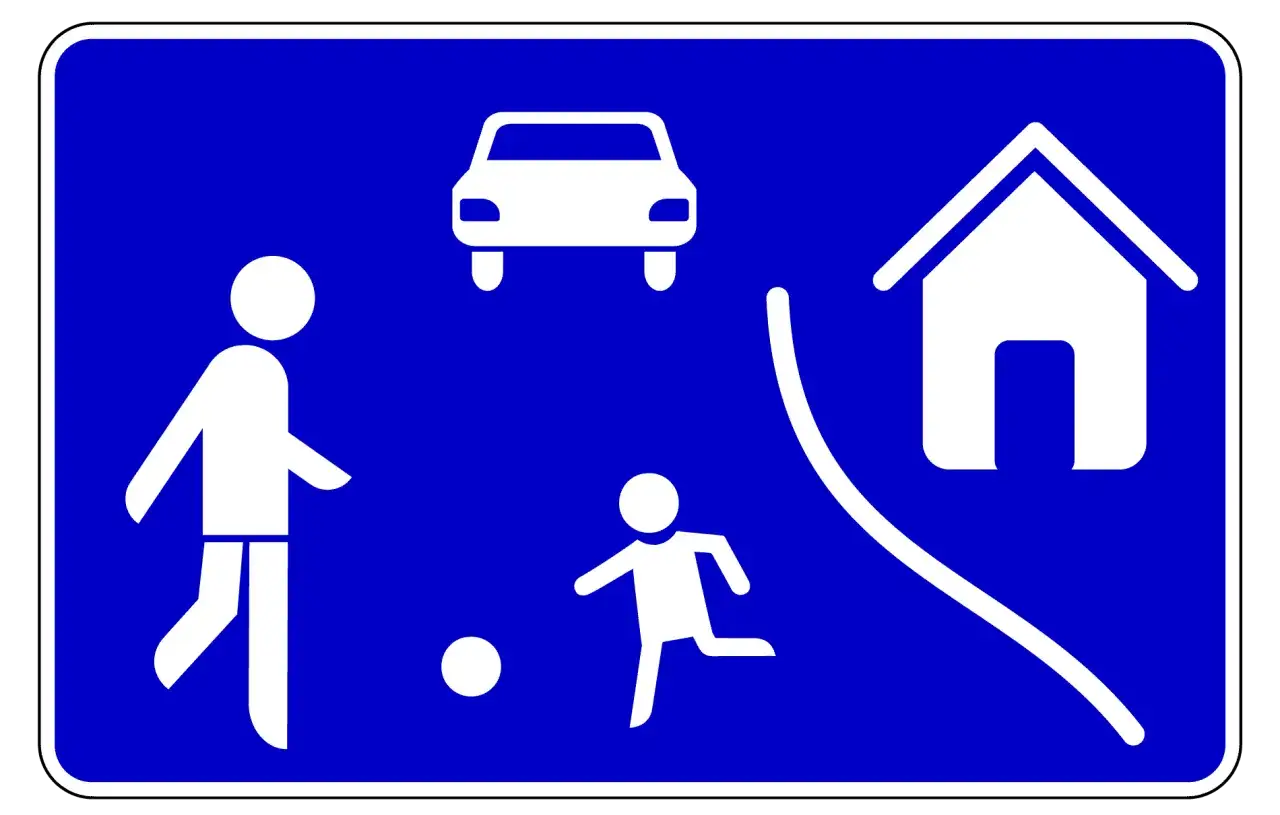 Verkehrsberuhigter Bereich StVO: Kinder spielen Fußball, ein Erwachsener schaut zu, ein Auto fährt langsam.
