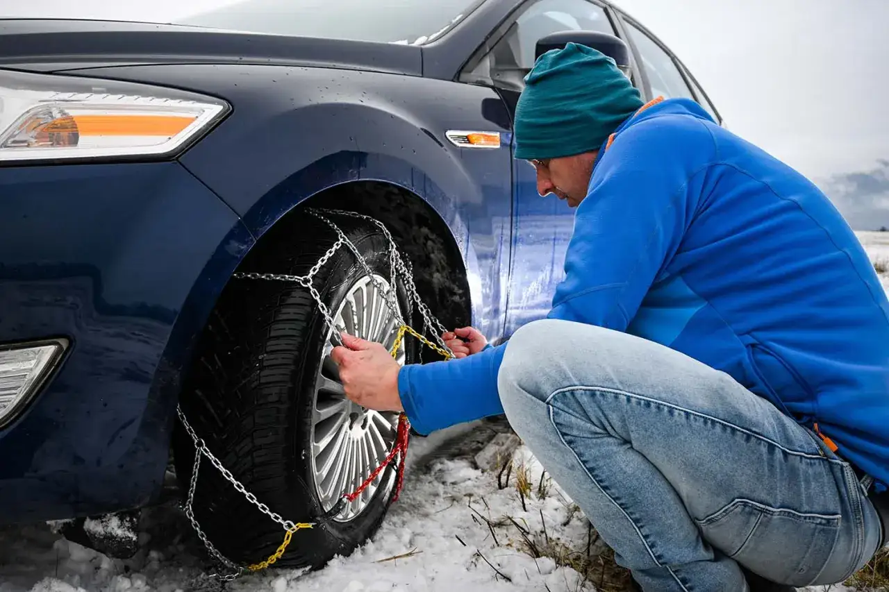 Mann montiert Schneeketten am Reifen. Wichtig für die Winterreifenpflicht in Italien bei Schnee und Eis.