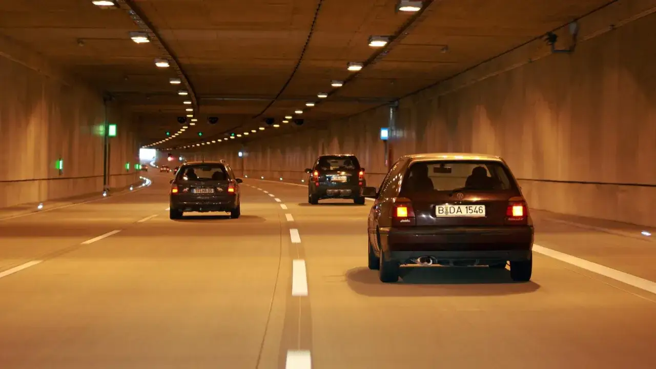 Autos fahren durch einen Tunnel, dessen Besonderheit die durchgehende Beleuchtung und die grünen Leuchten an den Wänden sind.