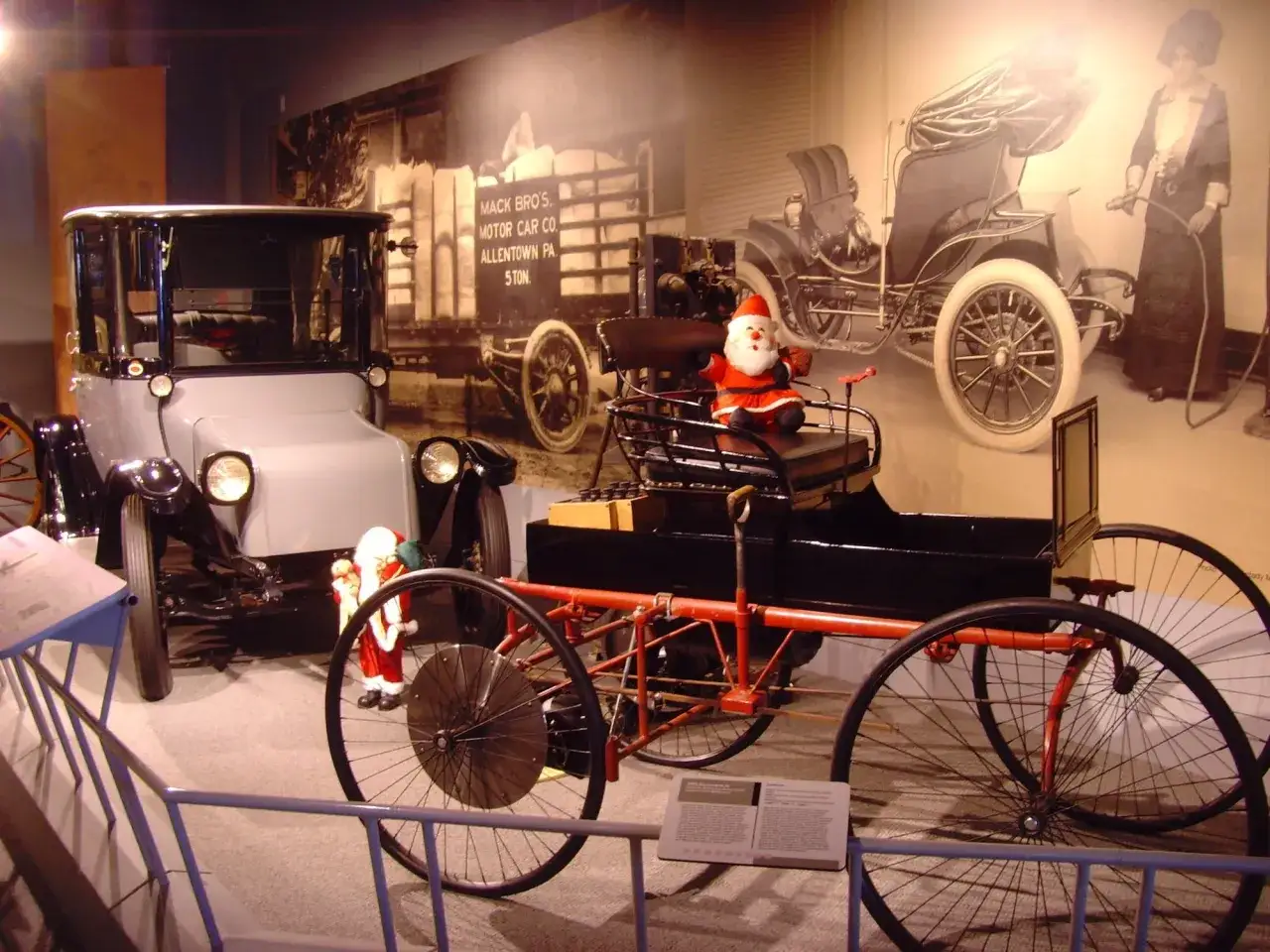 Old cars with automatic transmission: A 1900s Mack Bros. truck and a horseless carriage, with a Santa figure.