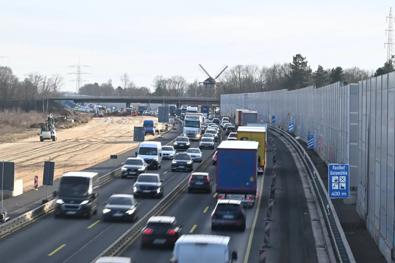 Langer Stau auf der A57 mit vielen Autos und LKW. Im Hintergrund ein Windrad und Baustellenfahrzeuge.