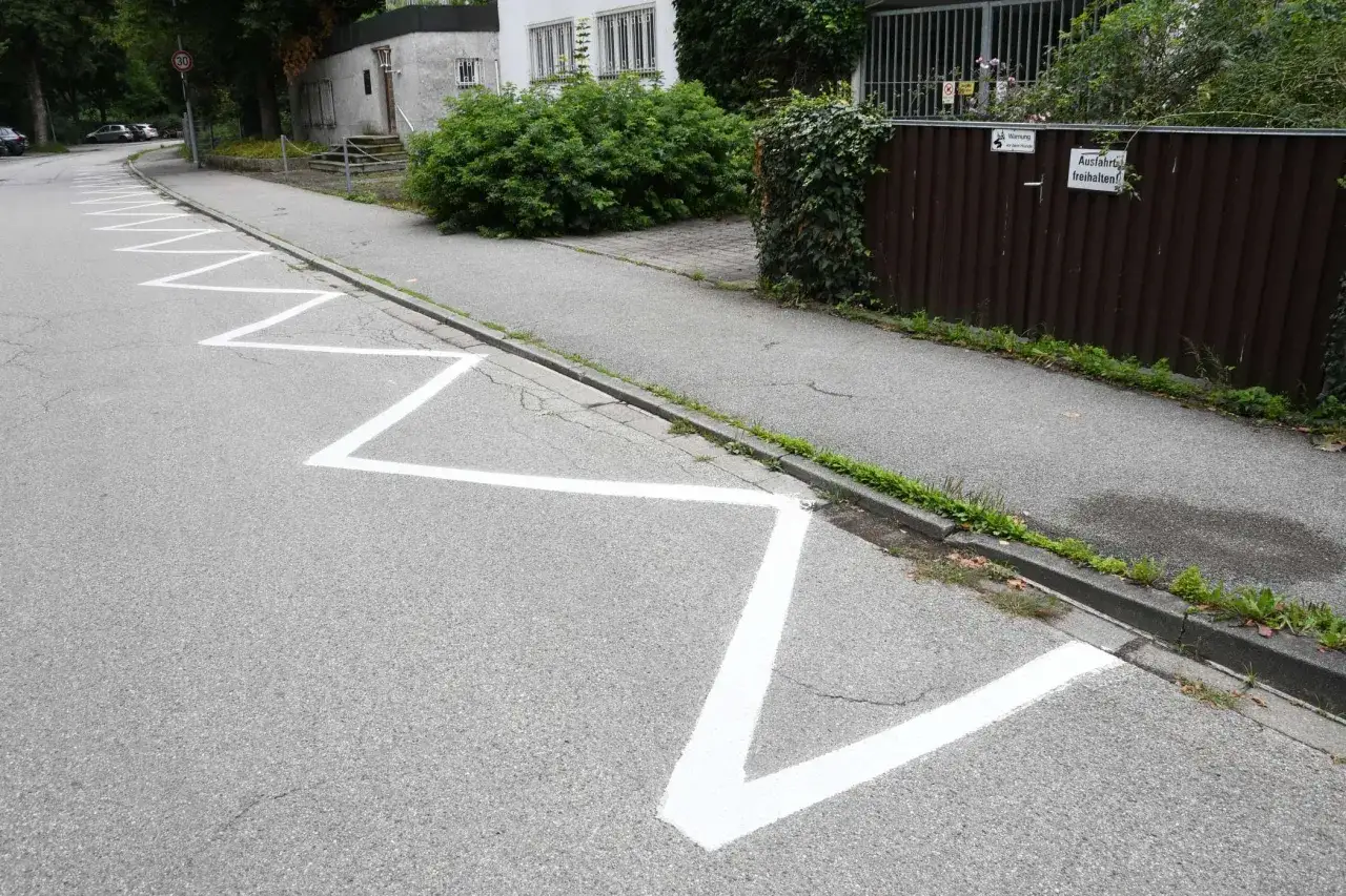 Zickzack-Markierungen auf der Straße zeigen an, wo das abgesenkter Bordstein parken erlaubt ist. Ein Schild weist auf eine Ausfahrt hin.