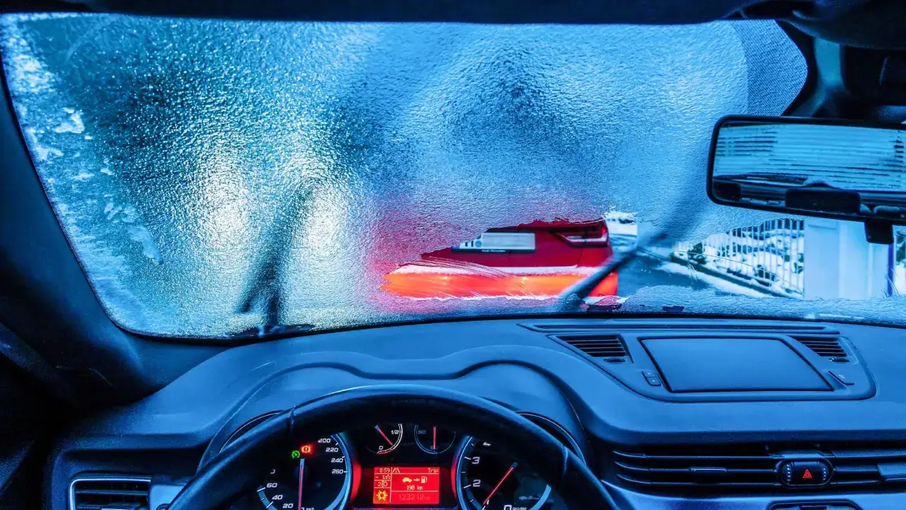 Eisige Scheibe, rotes Auto voraus. Der Motor läuft, um die Sicht freizubekommen.
