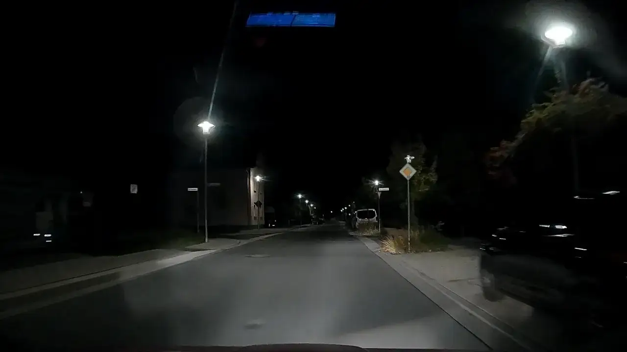 Nachtaufnahme einer Stra&szlig;e mit vielen Laternen, die wie blitzer ohne blitz leuchten. Ein Auto f&auml;hrt langsam.