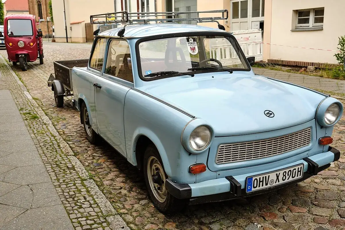 Hellblauer Trabant mit Anh&auml;nger und dem Kennzeichen OHV X 890H steht auf Kopfsteinpflaster.