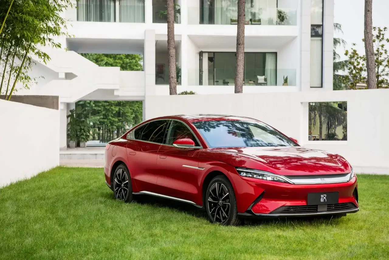 Roter BYD Han parkt auf einem gepflegten Rasen vor einem modernen wei&szlig;en Geb&auml;ude. Die Bedeutung von BYD liegt in seiner Vision f&uuml;r eine gr&uuml;nere Zukunft.