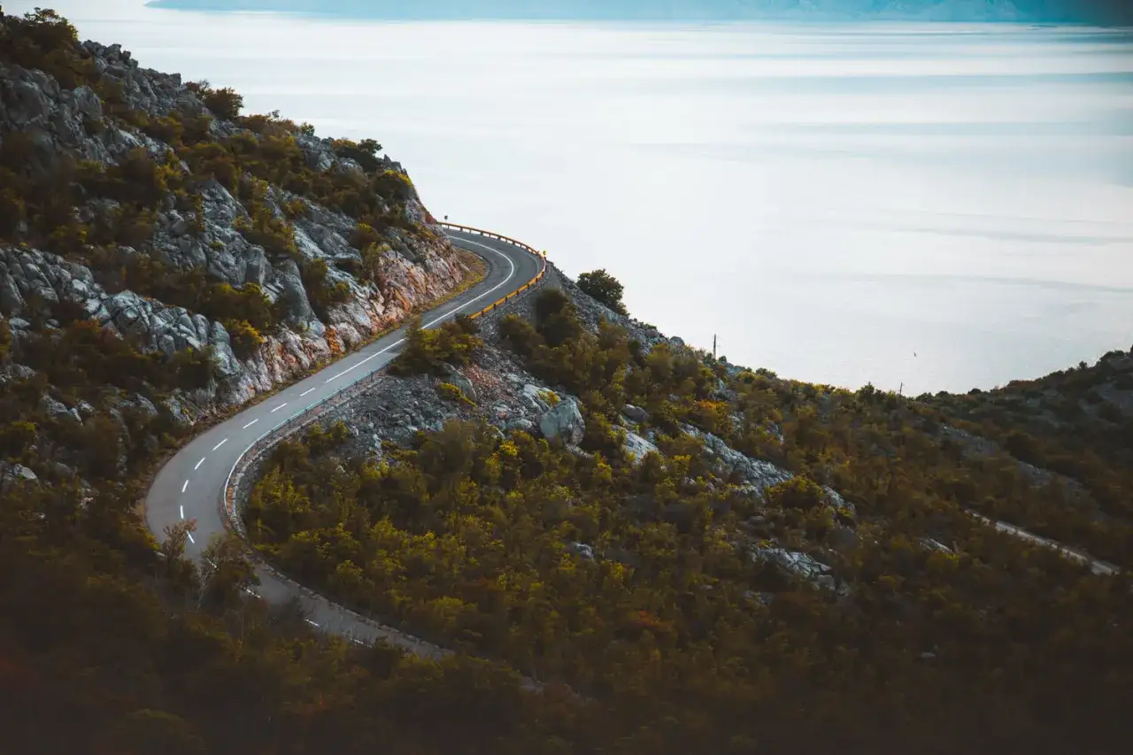 Kurvige K&uuml;stenstra&szlig;e auf der E71 in Kroatien, mit Blick auf das ruhige Meer und felsige H&auml;nge, bedeckt mit mediterraner Vegetation.