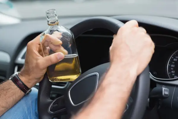 Mann hält Flasche Alkohol am Steuer. 2 Promille wieviel Alkohol? Gefährliche Fahrt.