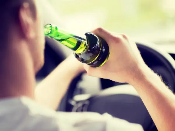Mann hält Flasche im Auto, ignoriert die Promillegrenze beim Autofahren.